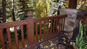 A wooden deck with a stone fireplace, a metal chair, and a potted plant.