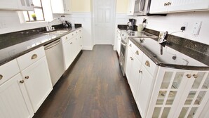 Une cuisine avec des armoires blanches, un plan de travail noir et un plancher en bois.