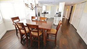 Un coin repas avec une table et des chaises en bois, un lustre et une cuisine en arrière-plan.