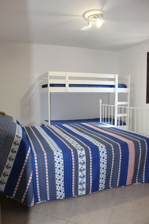 Ein Stockbett mit einer gestreiften Bettdecke in einem Zimmer mit weißen Wänden und einem Deckenventilator.