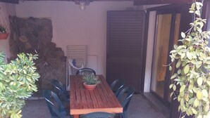 A wooden table with chairs, a potted plant, and a stone wall in a covered outdoor area. - MarVy house (Arbatax)