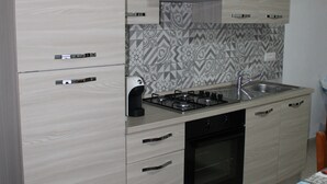 A modern kitchen with light wood cabinets, a stainless steel range hood, a built-in oven, and a patterned backsplash. - MarVy house (Arbatax)