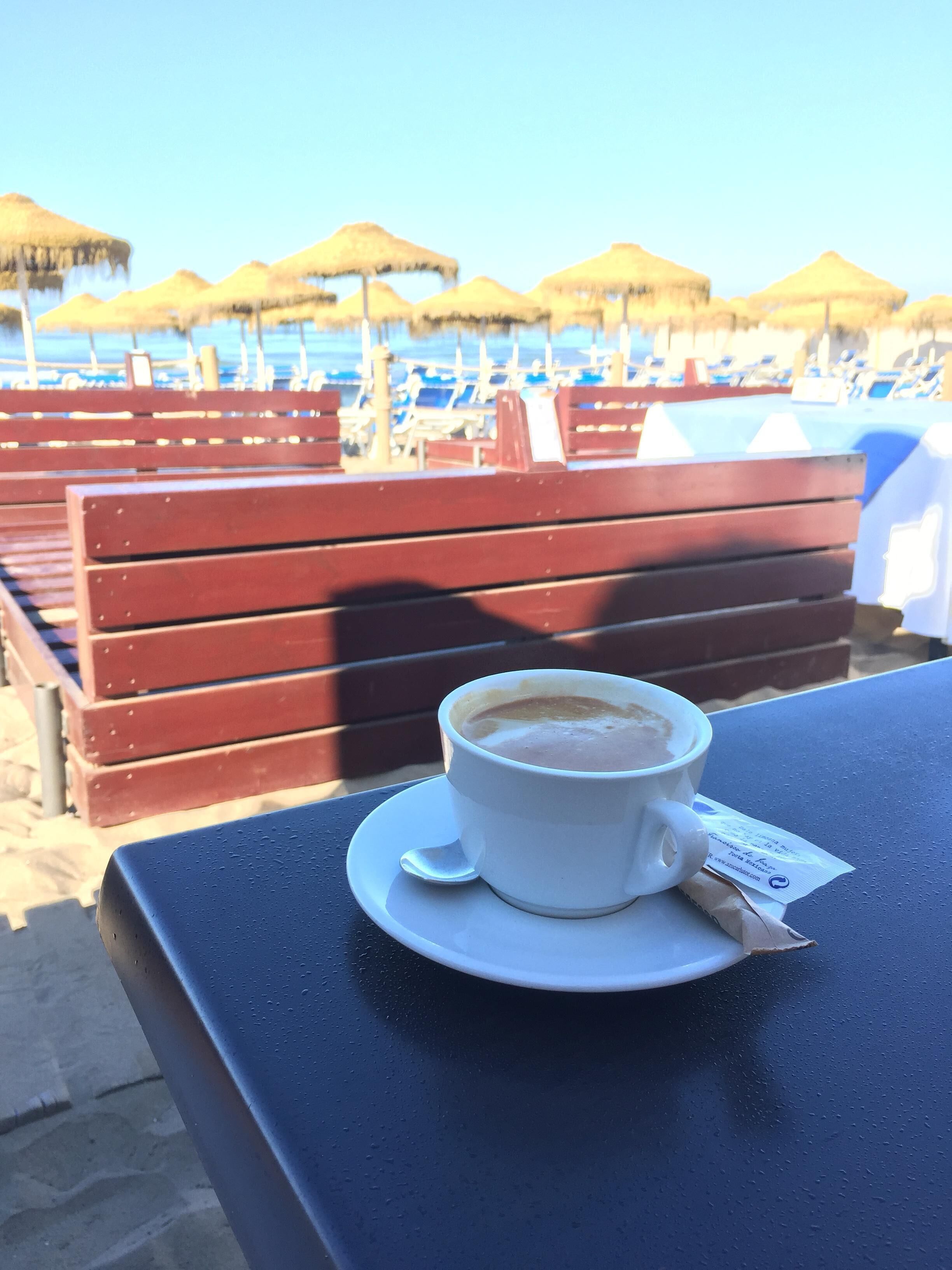 Een kop koffie op een tafel, met uitzicht op het strand.