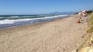 Une plage de sable avec des vagues, quelques personnes et des bâtiments en arrière-plan.