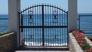 Une entrée pavée de pierres, avec un portail noir donnant accès à une vue sur la côte.