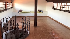 A spacious room with a wooden ceiling, a spiral staircase with ornate railings, and a seating area with cushions. - Casa De Praia Anequim (Cabo Frio)