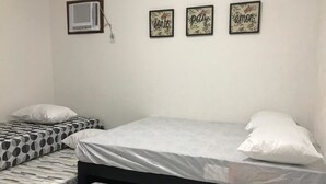 A bedroom with two beds, one with a polka dot bedspread and the other with a striped bedspread. There are three framed pictures on the wall, and an air conditioning unit is mounted on the wall. - Casa De Praia Anequim (Cabo Frio)