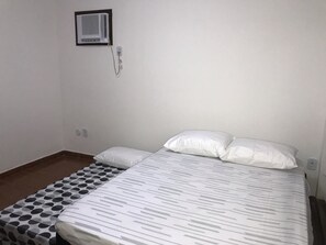 A single bed with a patterned bedspread and two pillows, a small bedside table, and a wall-mounted air conditioning unit.