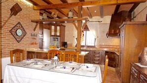 Zona pranzo con tavolo apparecchiato per quattro persone, sedie di legno, parete in mattoni e una cucina sullo sfondo.