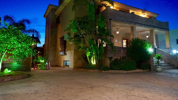 Una casa a due piani con un balcone, immersa nel verde e con un cortile lastricato.