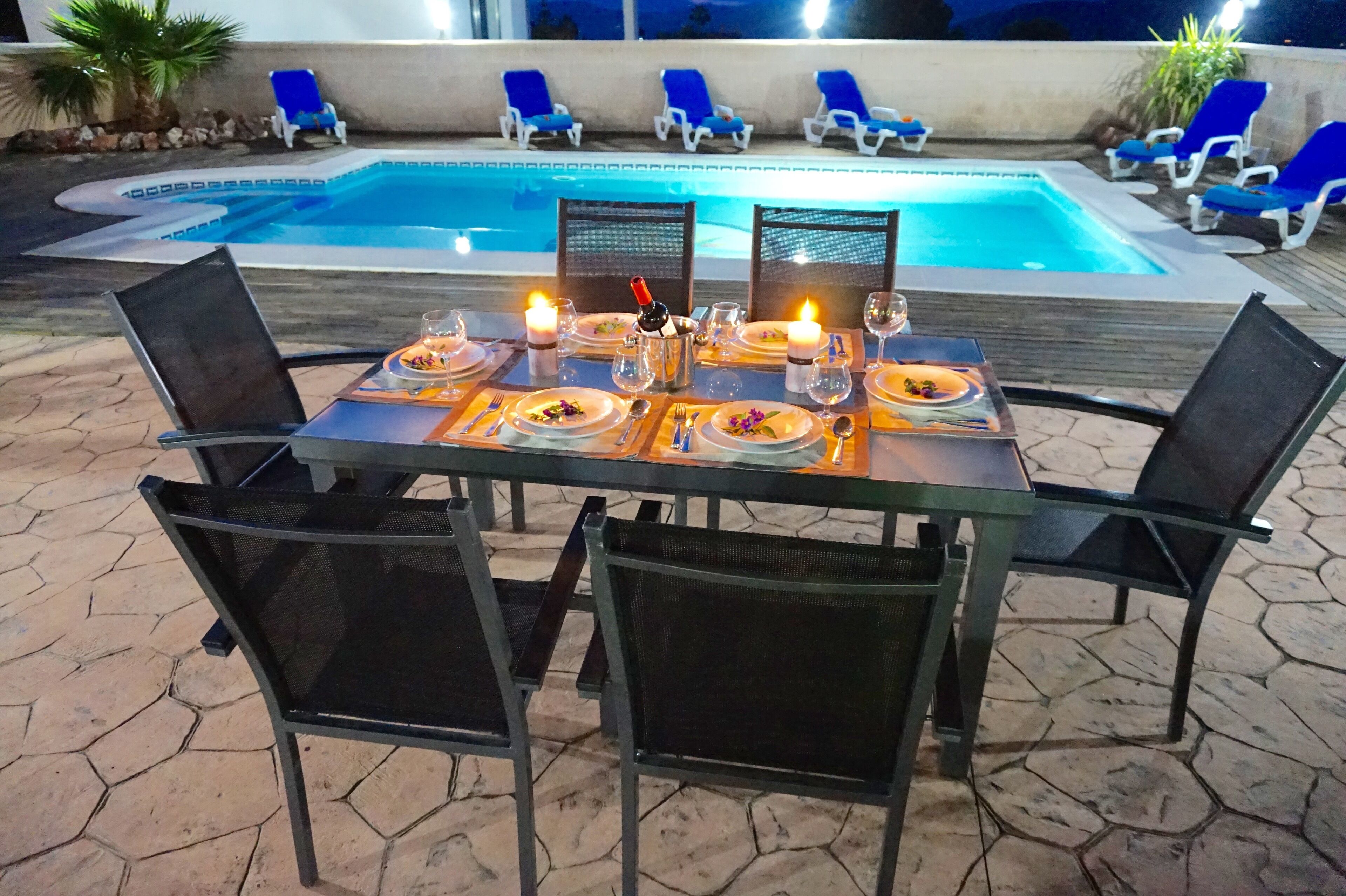 An outdoor dining area with a pool in the background.