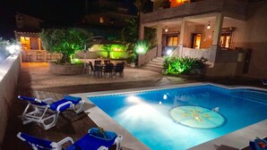 Una piscina con lettini e sdraio, circondata da un patio con posti a sedere all'aperto e piante.