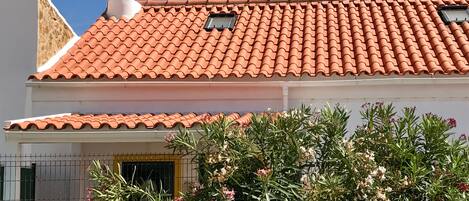 A building with a red-tiled roof, a white chimney, and a window with a metal grill.