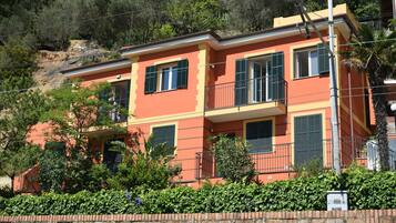 Un edificio a due piani con facciata in mattoni, diverse finestre con persiane e un balcone.