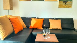 A living room with a black leather sofa, orange cushions, a small wooden coffee table with two wine glasses and a bottle, and three framed landscape paintings on the wall. - Large and bright, a stone's throw from the castle, balcony, FREE WIFI, A / C, parking space (Rimini)