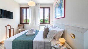 Una habitación de hotel con cama, una silla, un televisor, una ventana con cortinas y un cuadro en la pared.