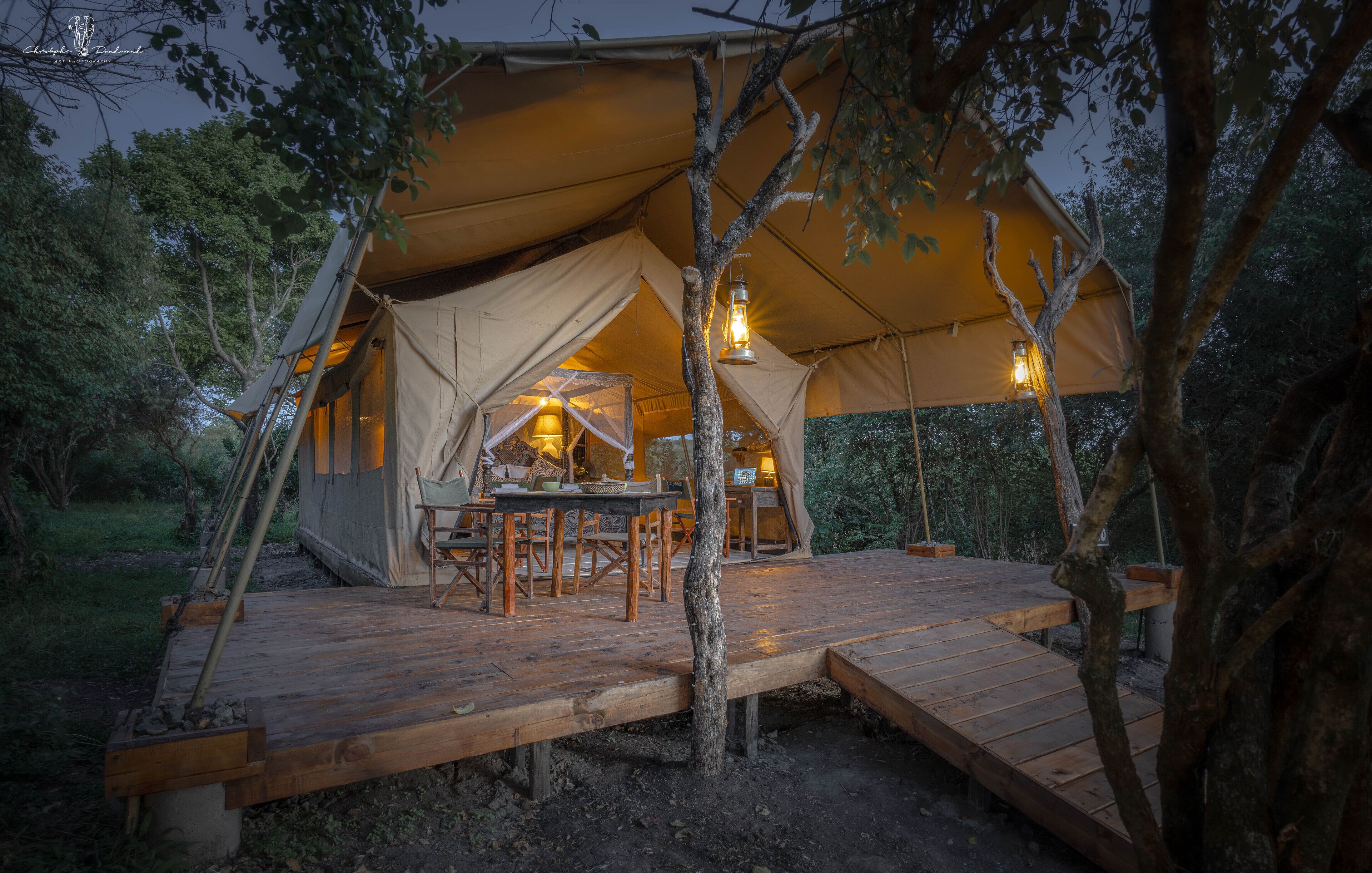 A tent with a wooden deck, a dining table, and two lanterns.