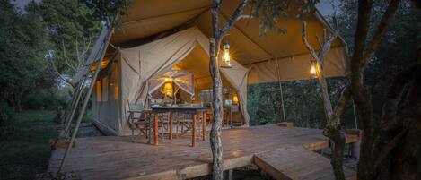 A tent with a wooden deck, a dining table, and two lanterns.