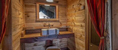 A wooden cabin bathroom with a window, wooden bench, and a hanging light fixture.