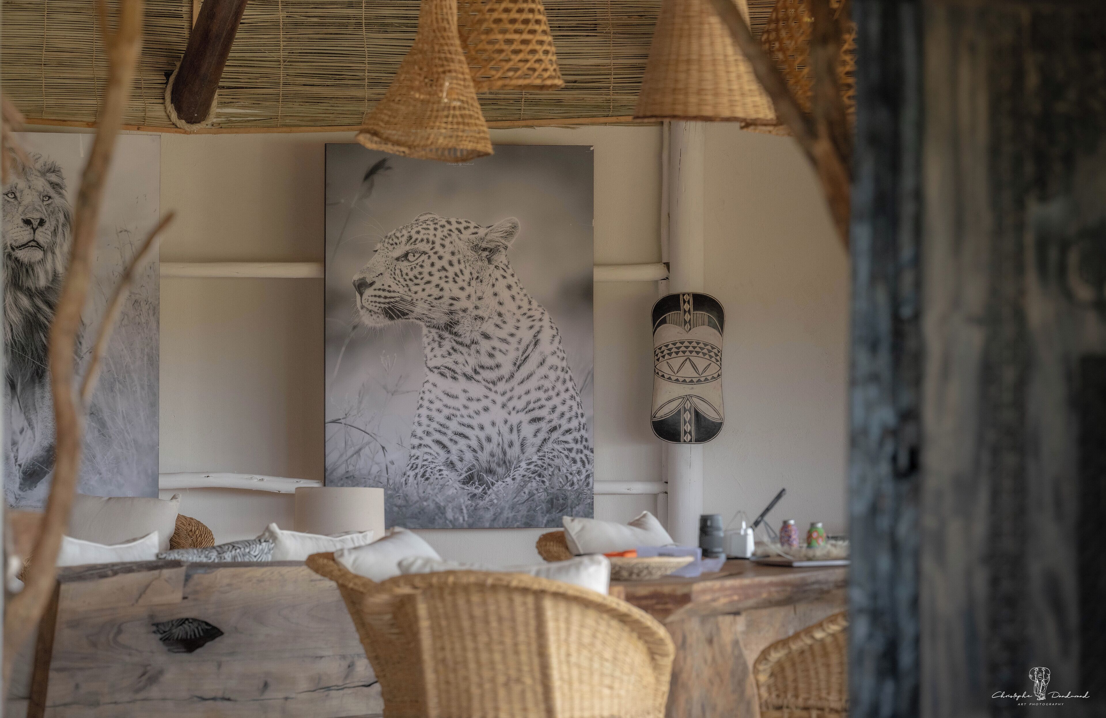 Un comedor con sillas de mimbre, una mesa con mantel blanco y un cuadro grande de un leopardo en la pared.
