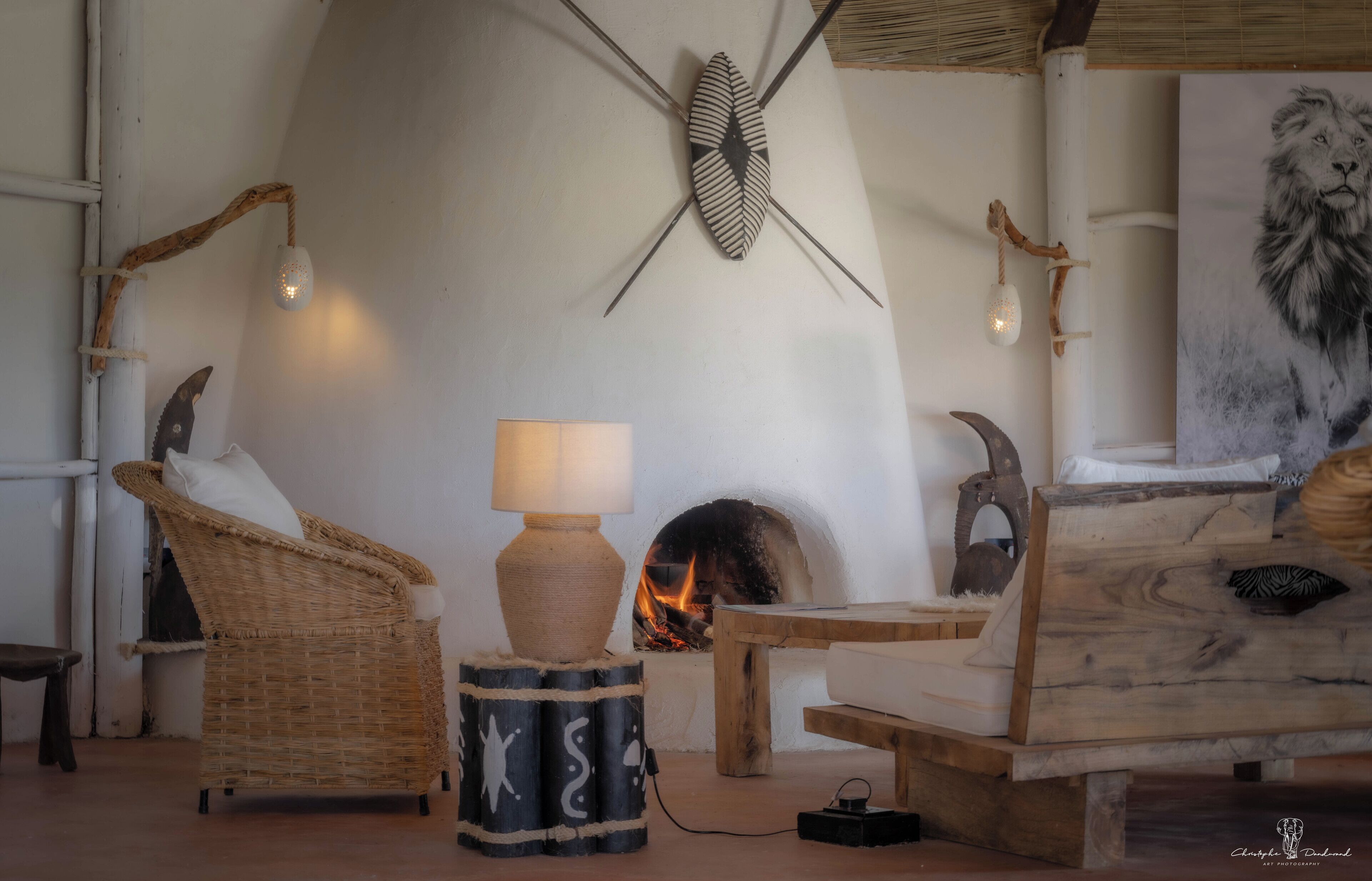 Une pièce chaleureuse avec une cheminée, des meubles en osier et une lampe à motifs zébrés.
