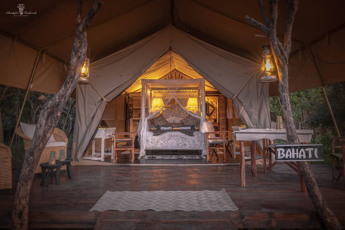 Alojamiento en carpa con cama, mesas, sillas y un letrero que dice "BAHATI".