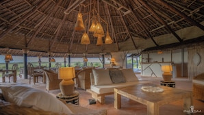 Un salón de planta abierta con techo de paja, mobiliario de mimbre y lámparas colgantes.