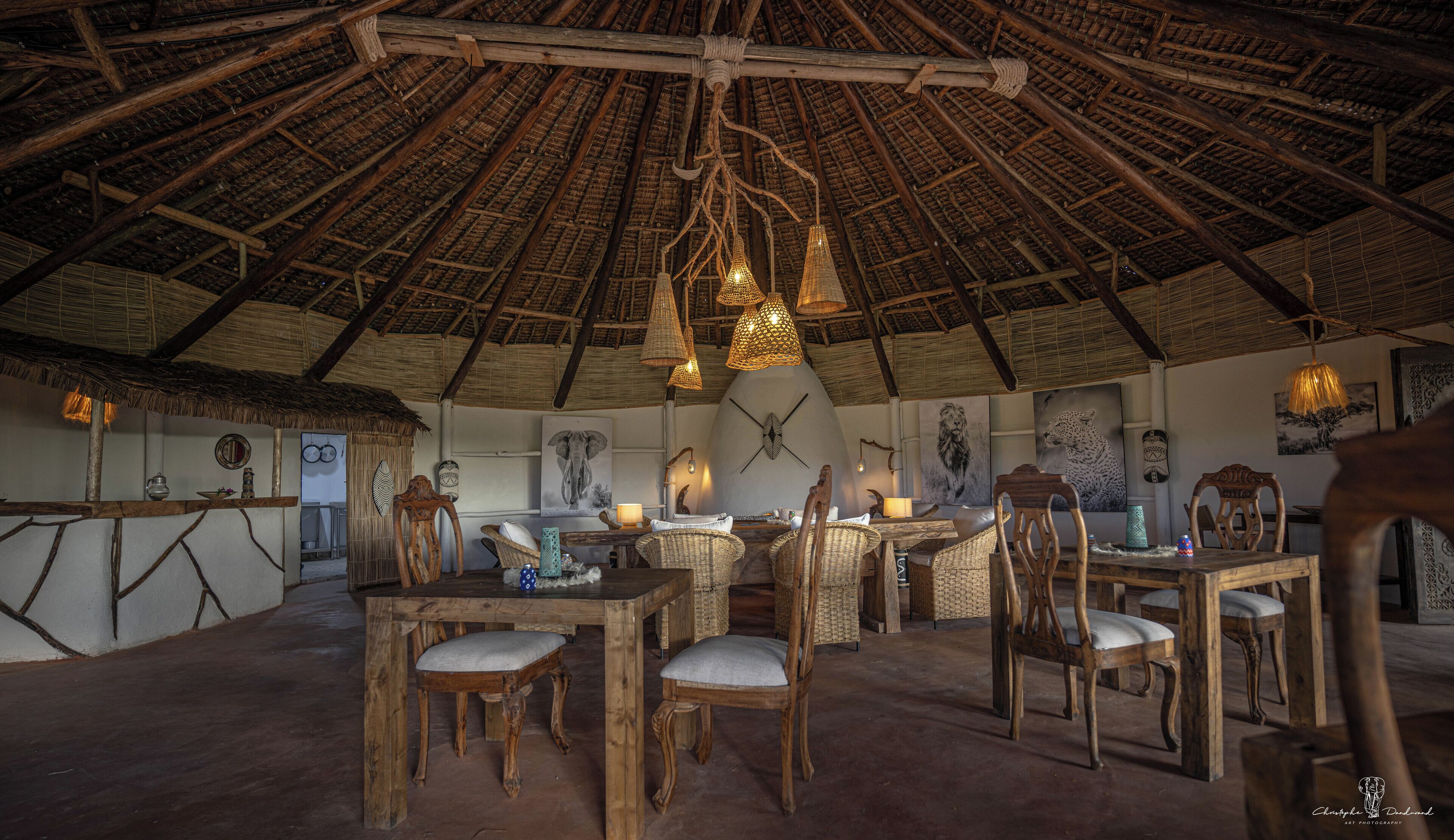 A rustic interior with a thatched roof, wooden furniture, and woven light fixtures.