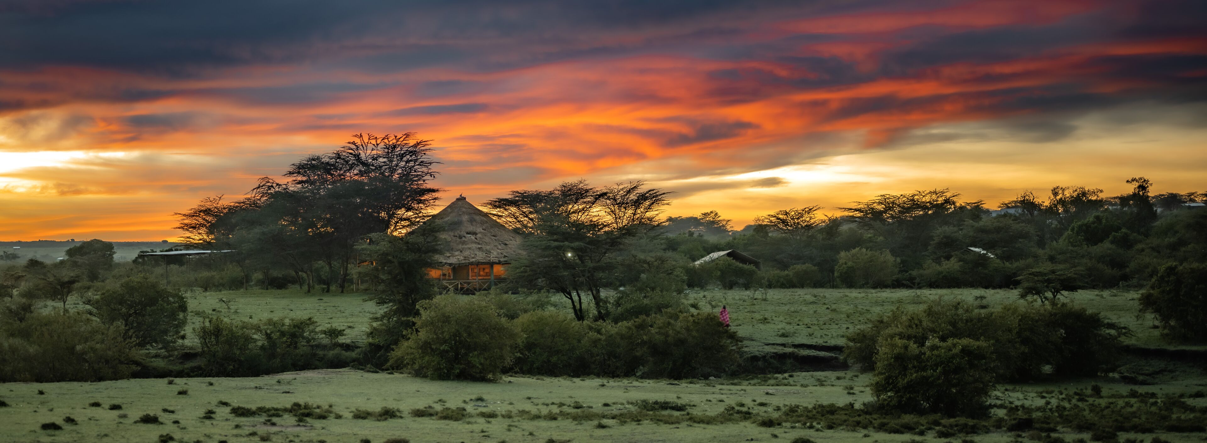 A rural landscape with a thatched-roof house surrounded by greenery and a sunset sky.