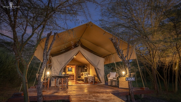 Alojamiento con carpa, una terraza de madera, un comedor y un letrero que dice "KAZURI".