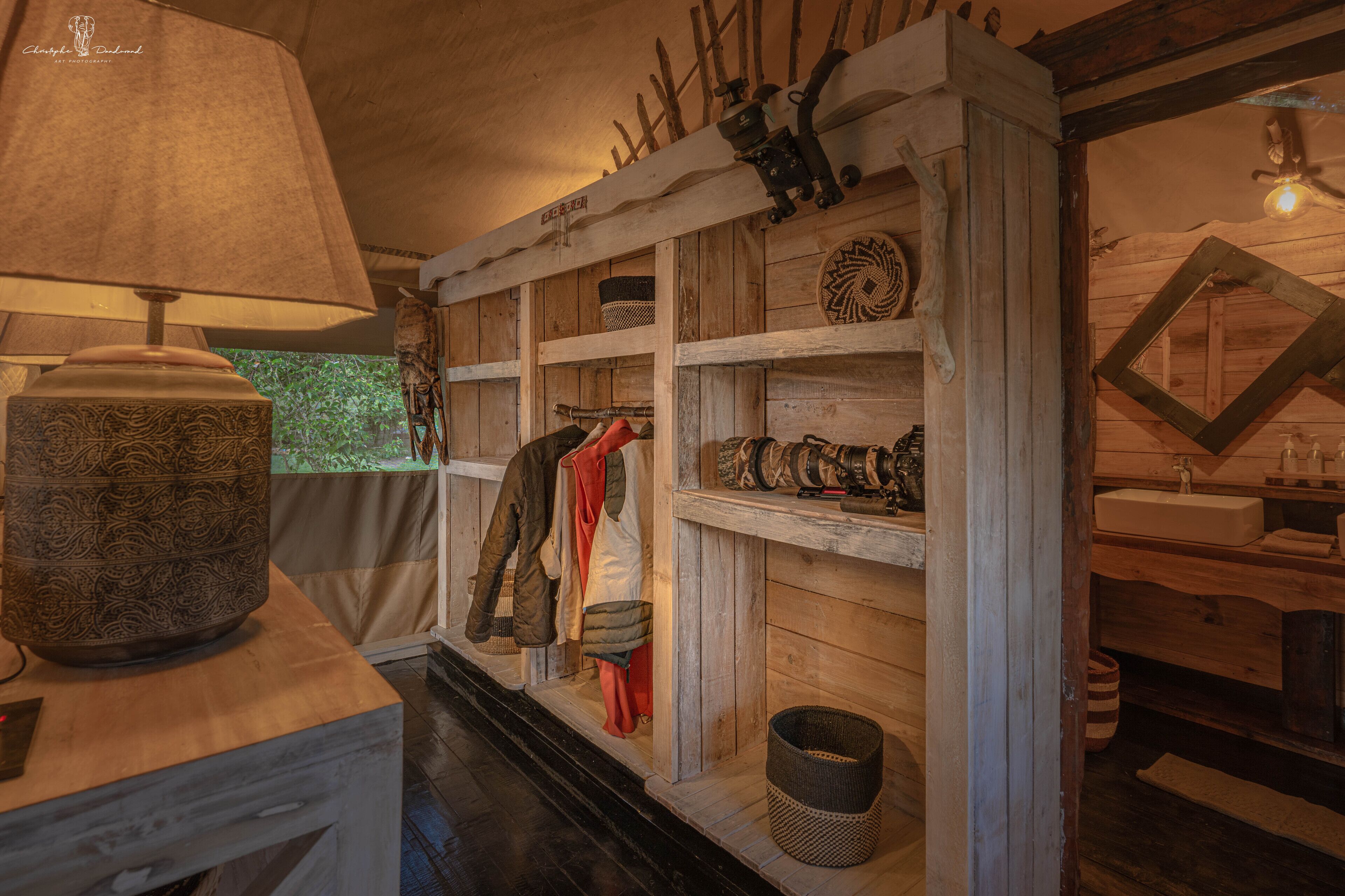 A rustic wooden interior with shelves displaying clothing and accessories, a lamp, and a wooden bench.