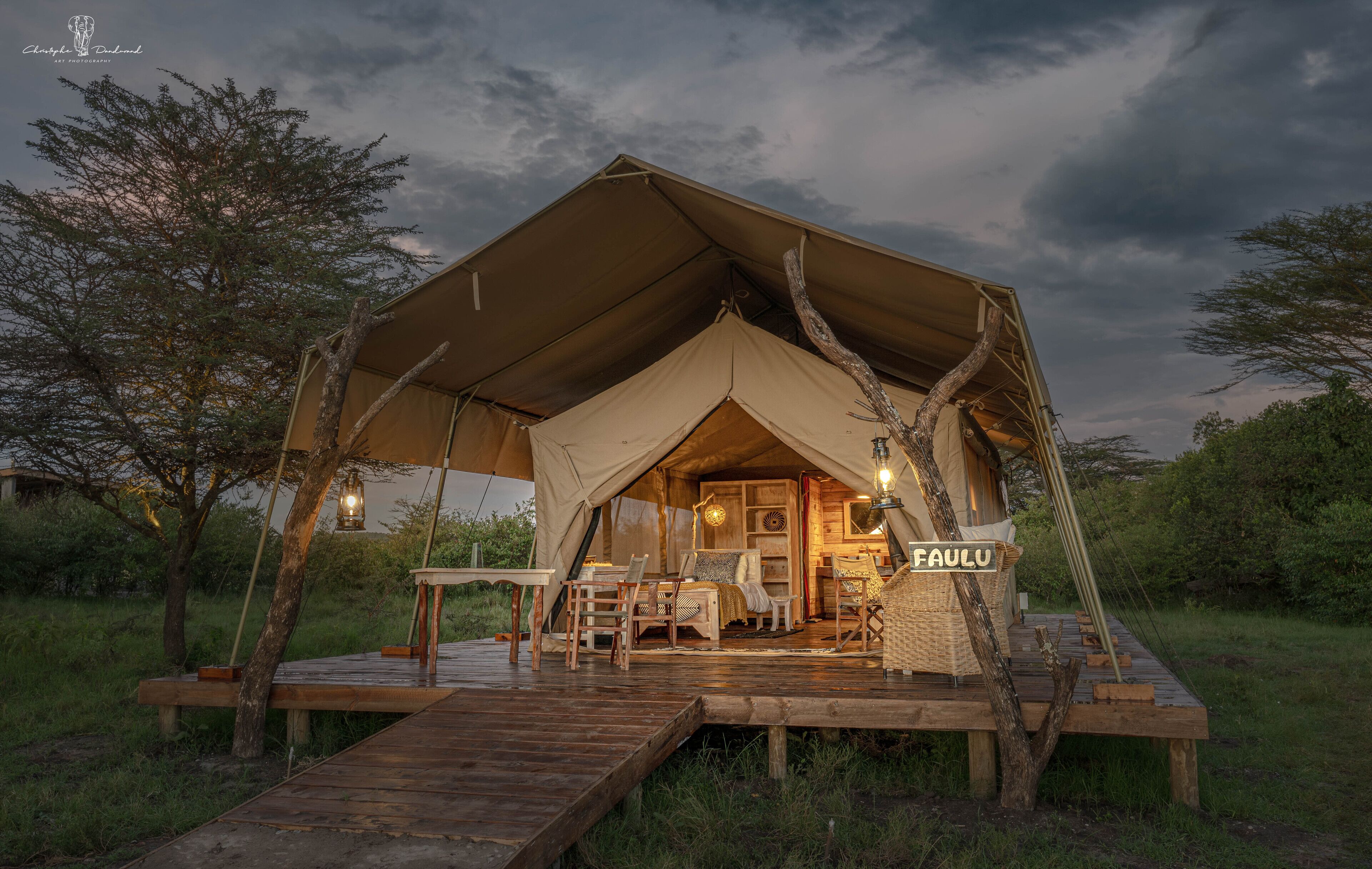 A tented accommodation with a wooden deck, interior lighting, and a sign reading "FAULU".
