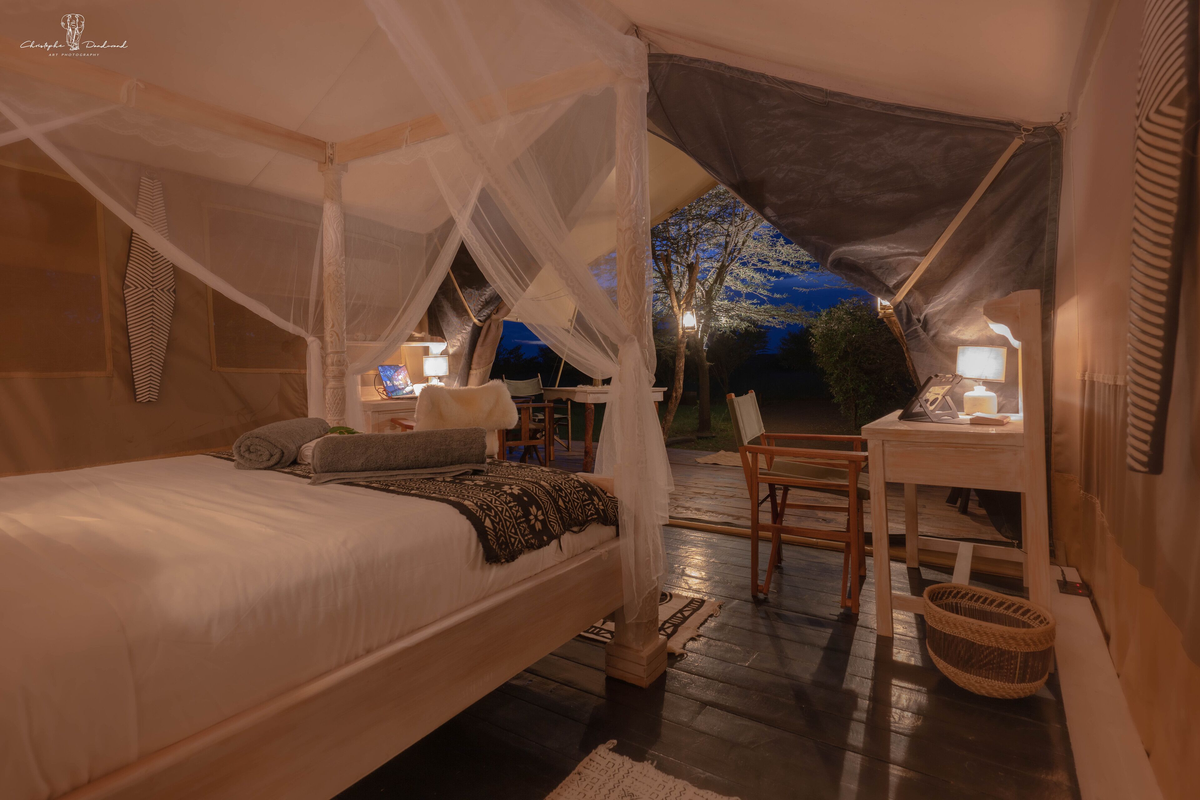 A tented accommodation with a bed, bedside table, and a chair.