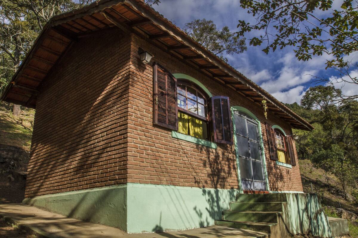 A brick house with a green base, a wooden roof, and a window with shutters.