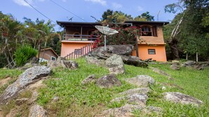 A two-story house with a satellite dish, surrounded by rocks and greenery. - Pousada Céu de Luz - Próximo a Monte Verde (Itapeva)