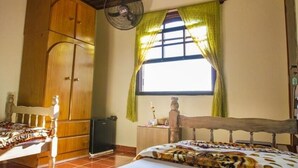 A bedroom with a wooden bed, a wardrobe, a window with curtains, and a ceiling fan. - Pousada Céu de Luz - Próximo a Monte Verde (Itapeva)