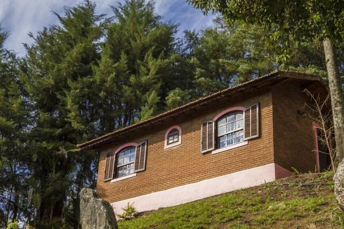 A two-story brick house with a sloped roof, surrounded by dense trees.
