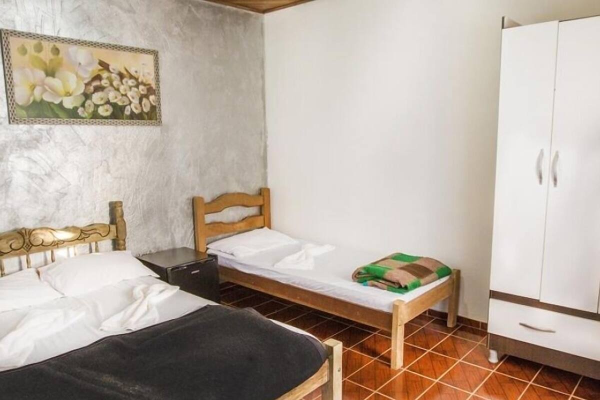 A bedroom with two beds, a wardrobe, and a painting on the wall.