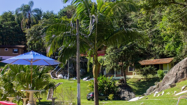 Una piscina con una sombrilla azul, palmeras y una casa al fondo.
