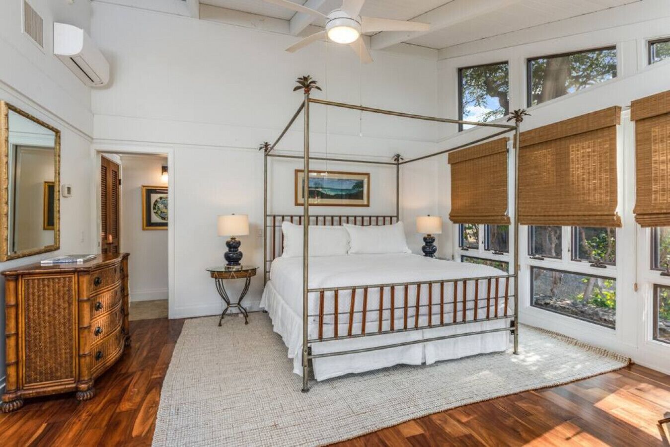 Una cama con dosel y vistas al exterior, un aparador de madera y una mesita con una lámpara.