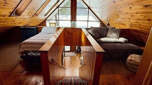 A cozy attic bedroom with a sloped ceiling, wooden walls, a bed, a sofa, and a small table.