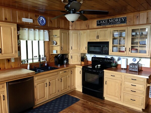 A kitchen with wooden cabinets, a black stove, a microwave, and a ceiling fan.