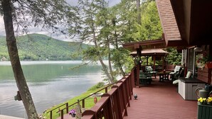A wooden deck with outdoor seating, overlooking a lake and forested hills.
