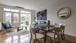 Relax in this stylish living room with a comfortable sofa, coffee table, and dining area, leading to an outdoor space with a deck and potted plants.