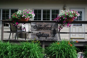 Puinen kyltti, jossa lukee ”Woodland Cottage”, ja sen ympärillä on ruukuissa olevia kukkia ja vihreitä kasveja.