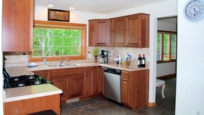 Une cuisine avec des meubles de rangement en bois, une cuisinière, un lave-vaisselle et une fenêtre donnant sur les arbres.