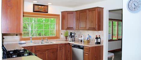 A kitchen with wooden cabinets, a stove, a dishwasher, and a window with a view of trees.