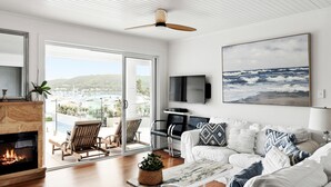 Una sala de estar moderna con chimenea, televisor grande y un área de estar confortable con vista al mar.