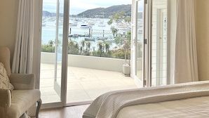 Un dormitorio con cama, ventilador de techo y vista a un puerto deportivo a través de amplios ventanales.