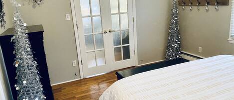 Un dormitorio con cama, una puerta blanca con paneles de vidrio esmerilado, dos apliques en la pared, un perchero con ganchos y una unidad de aire acondicionado pequeña en la pared.